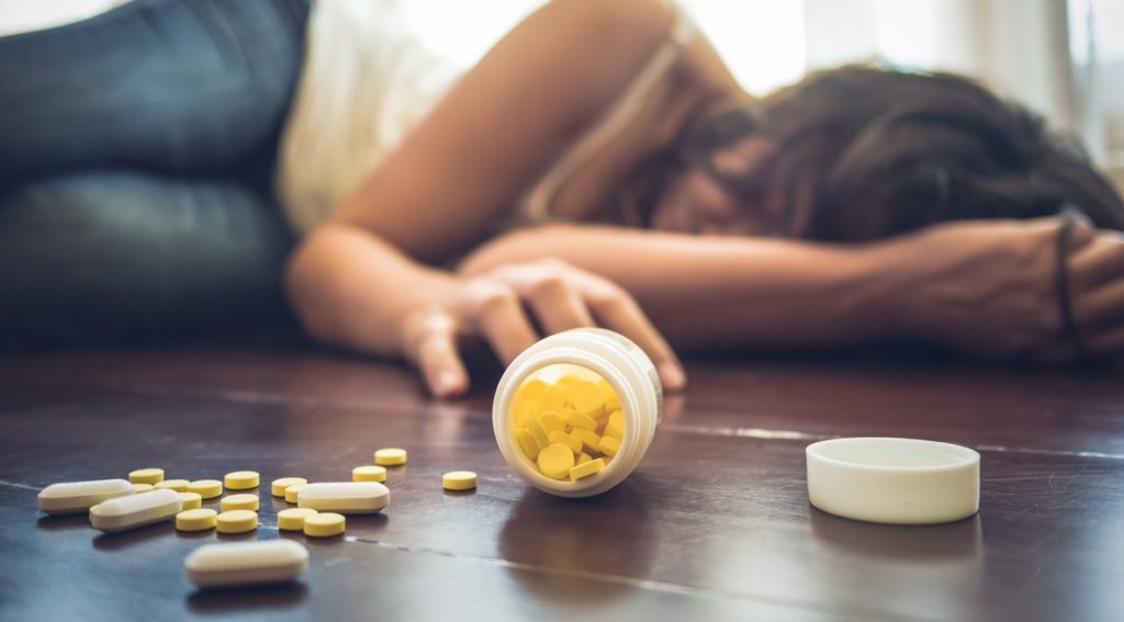 Woman taking medicine overdose and lying on the wooden floor with open pills bottle. Concept of overdose and suicide.